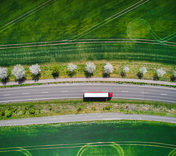 Truck driving on road, surrounded by green lands, viewed from the top
